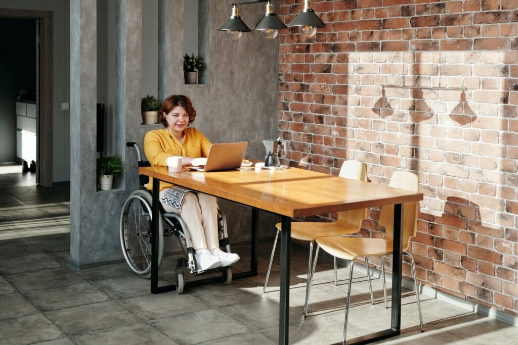 Shows a woman in a heelchair working at a table on a laptop