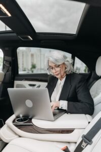 An older lady working on a laptop from inside a car