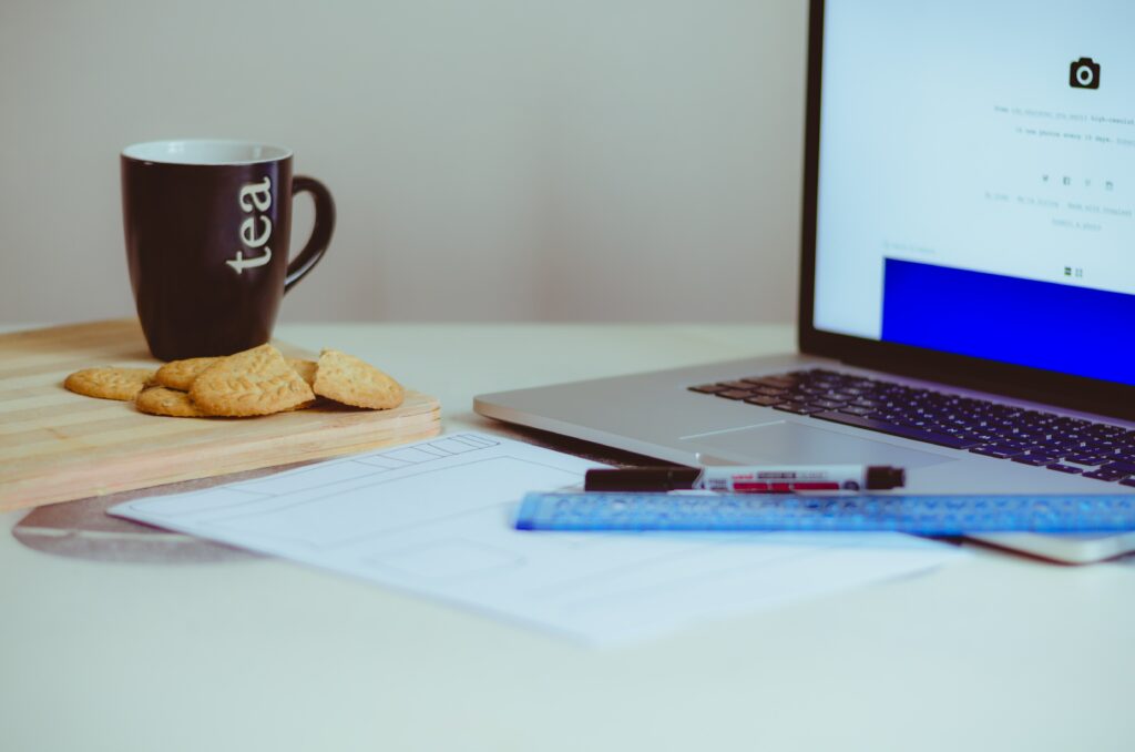 A mug and some biscuits positioned beside a laptop.